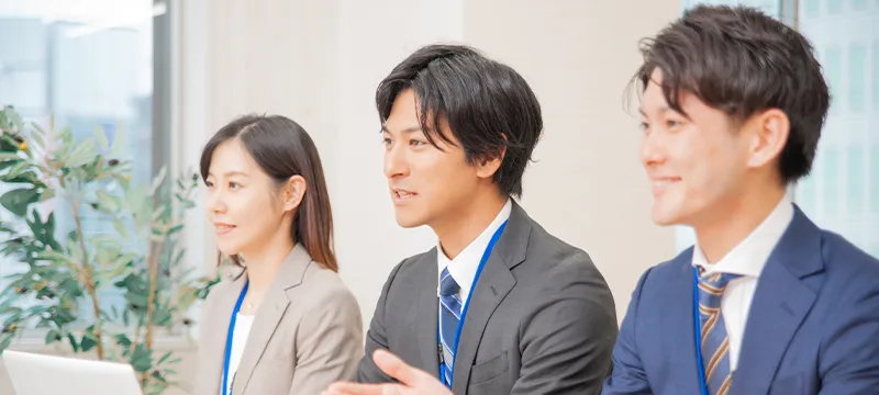 スーツの男性2人と女性1人が並んで座っている