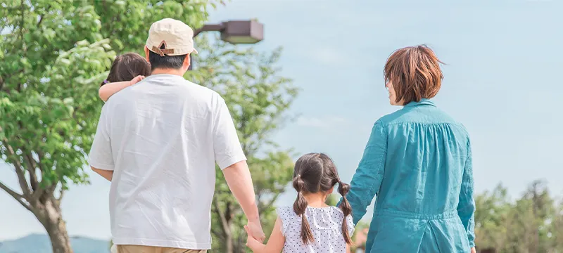 手をつないで公園を歩く四人家族の後ろ姿
